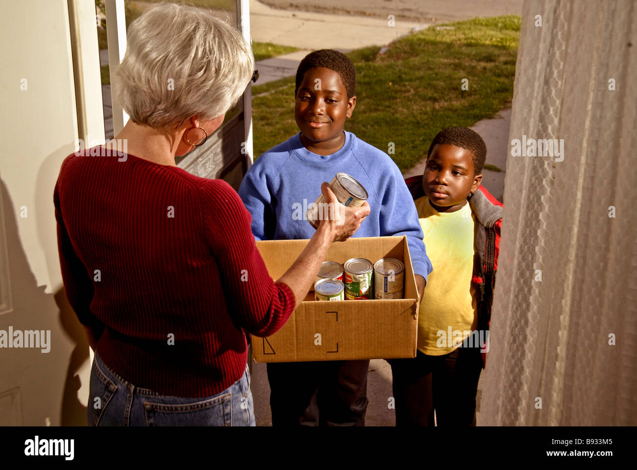 Due americano africano fratelli di età compresa tra i sette e i dieci raccogliere cibo inscatolato per una chiesa della carità da un bianco di casa in California Foto Stock