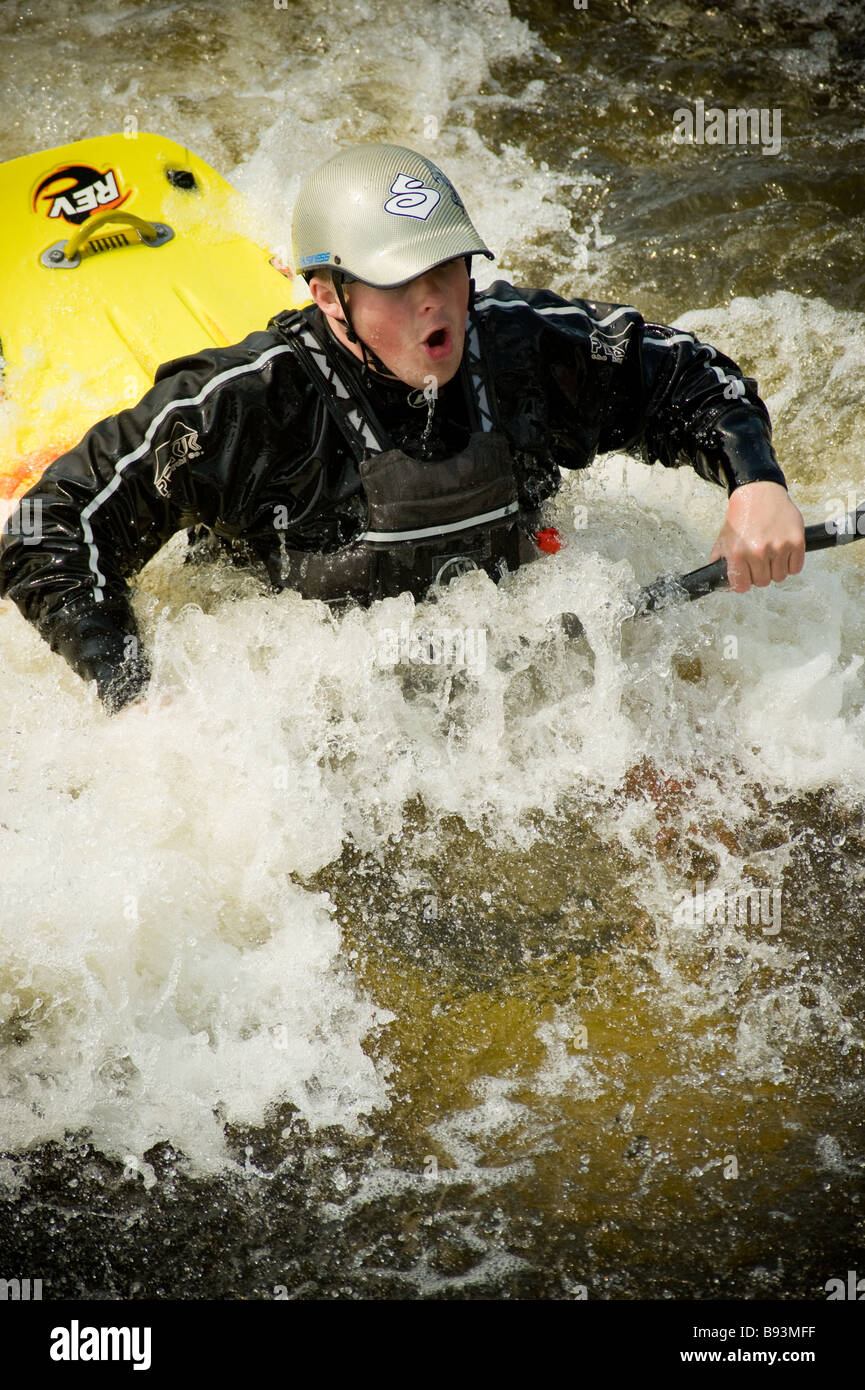 Giovane kayaker maschio caucasico che esegue un trucco con la prua del suo kayak sommerso in acqua al Tees Barrage International White Water Centre. REGNO UNITO Foto Stock