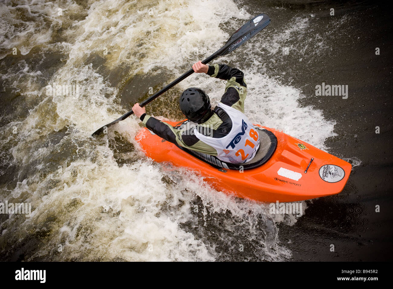 Vista posteriore rialzata di un kayak che indossa un casco di sicurezza e un supporto per la galleggiamento in gara presso il Tees Barrage International White Water Centre. REGNO UNITO Foto Stock