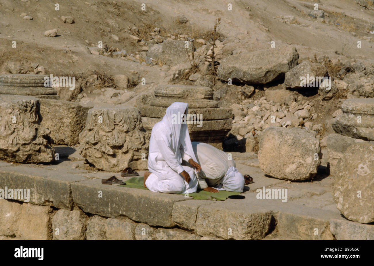 La Giordania Medio Oriente Jerash due uomini musulmani inginocchiati in rovine archeologiche a pregare verso la Mecca. Foto Stock