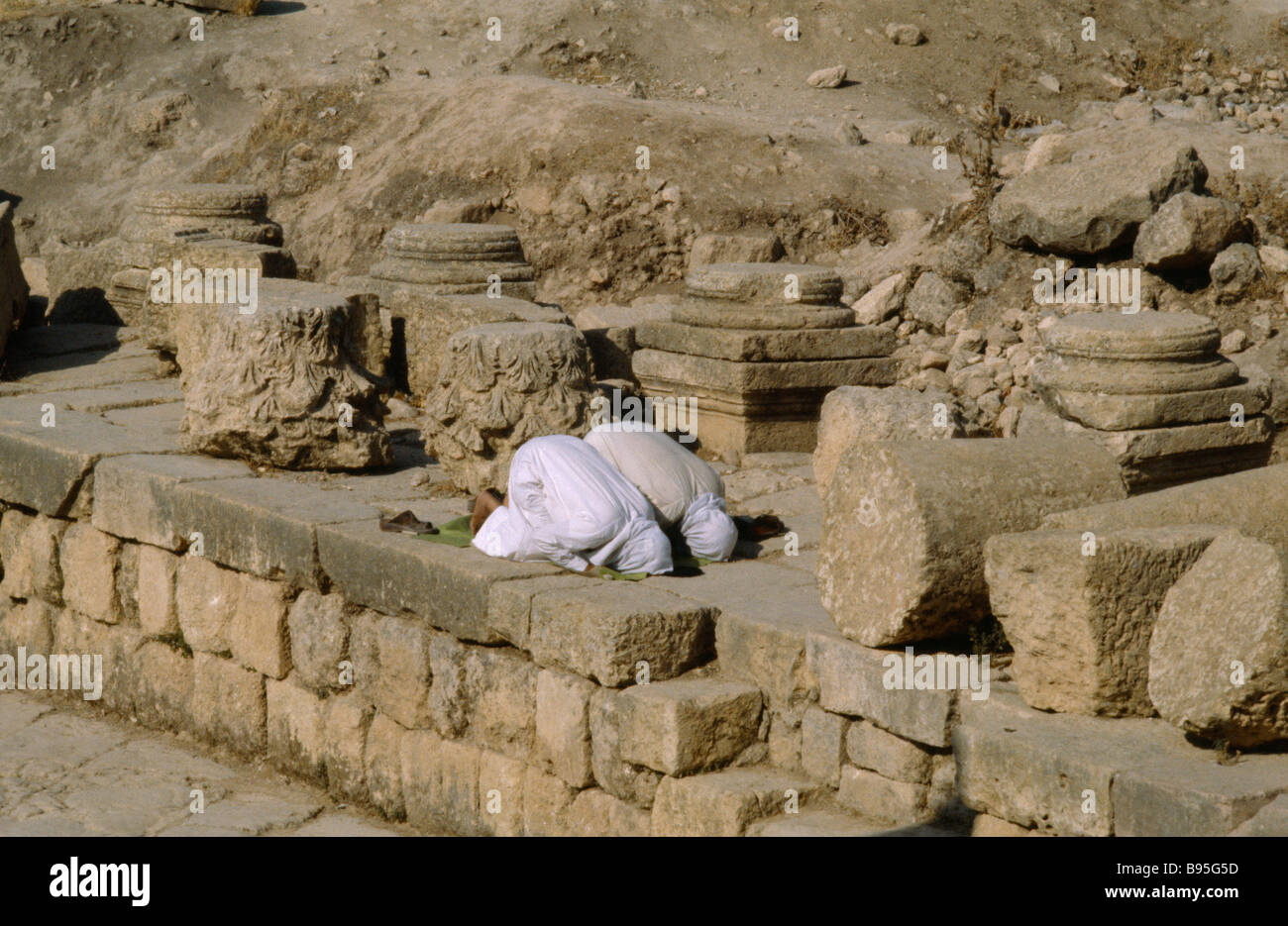 La Giordania Medio Oriente Jerash due uomini musulmani inginocchiati in rovine archeologiche a pregare verso la Mecca. Foto Stock