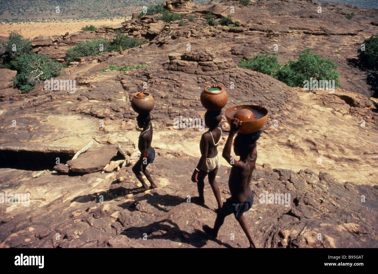 MALI paga il popolo Dogon Dogon boys portando vasi d'acqua sulle loro teste su terreno roccioso. Foto Stock