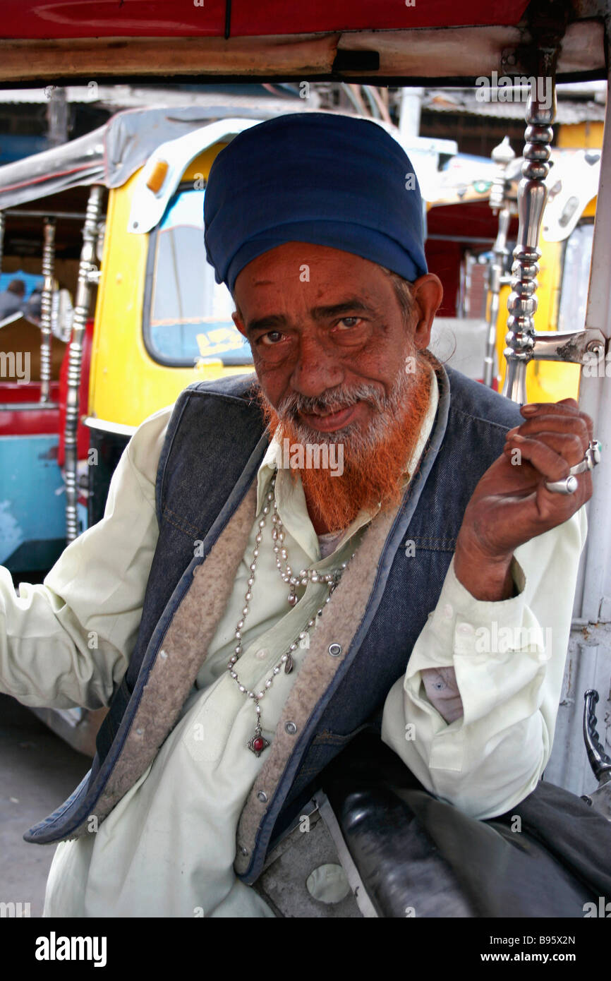 INDIA Delhi Nuova Delhi ritratto di auto rickshaw driver interno veicolo con tinte rosso barba anelli d'argento e collana. Foto Stock