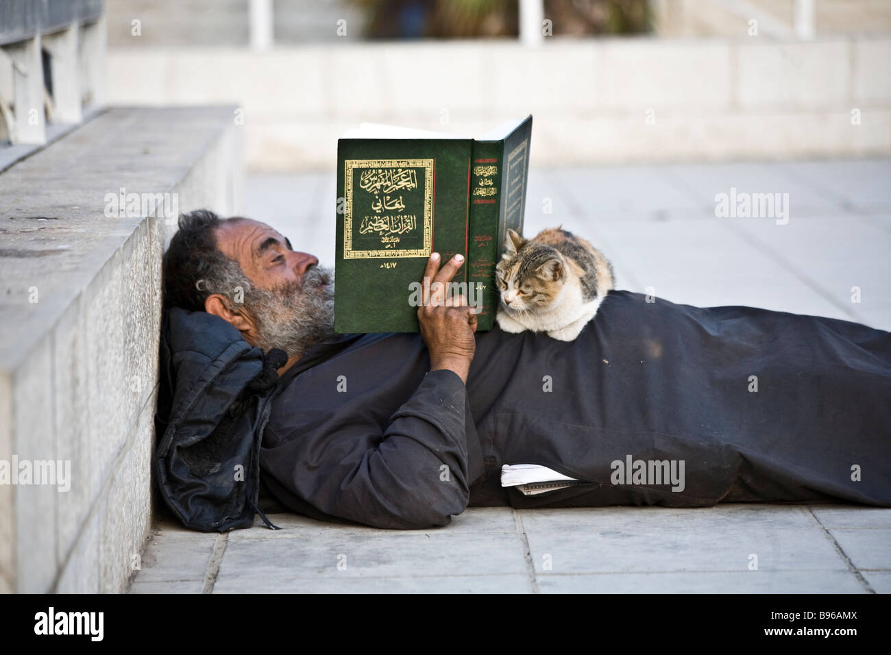 Colpo di un uomo nel centro di Amman in Giordania, disteso sul marciapiede la lettura del Corano. Il suo gatto pazientemente giace sul suo stomaco. Foto Stock