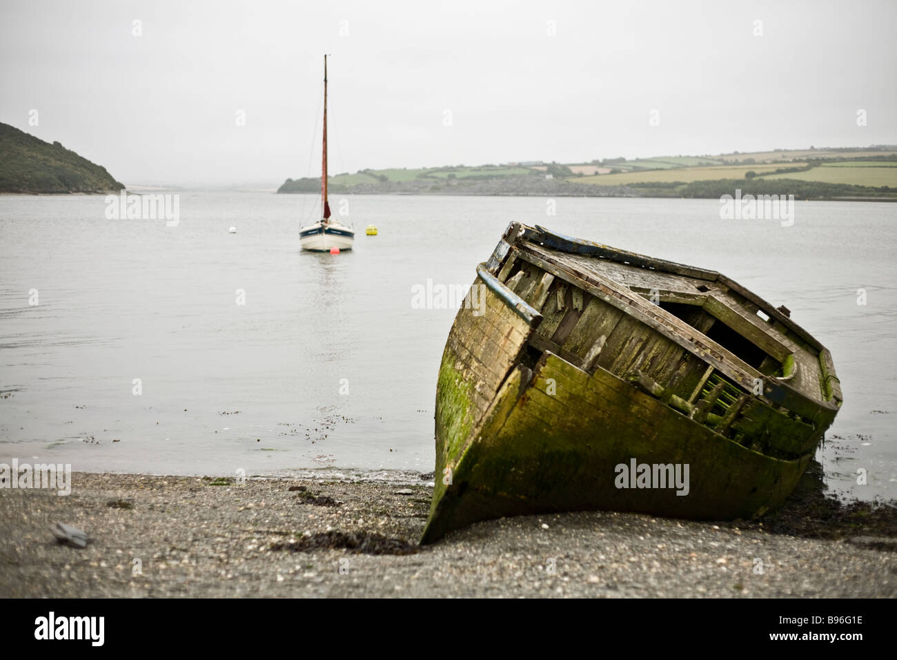 Devastata nello scafo di una vecchia barca da pesca con un moderno yacht in background. Prese sulla banca del fiume di cammello al di fuori di Padstow. Foto Stock