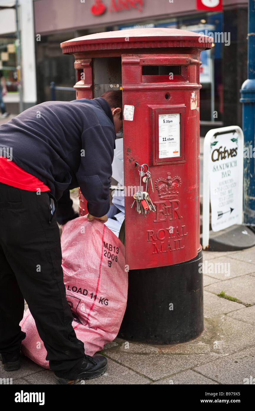 Femmina lavoratore postale la raccolta di lettere da parte di un rosso post office casella montante Aberystwyth Wales UK Foto Stock