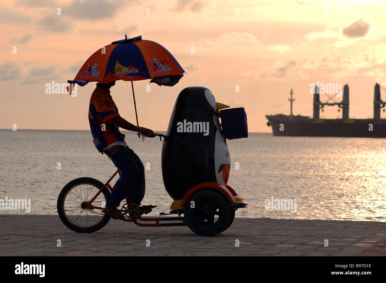 Penguin ice cream venditore bicicletta triciclo spiaggia tramonto waterfront marchio ombrello Santa Marta Colombia mare dei Caraibi Bonice lavoro Foto Stock