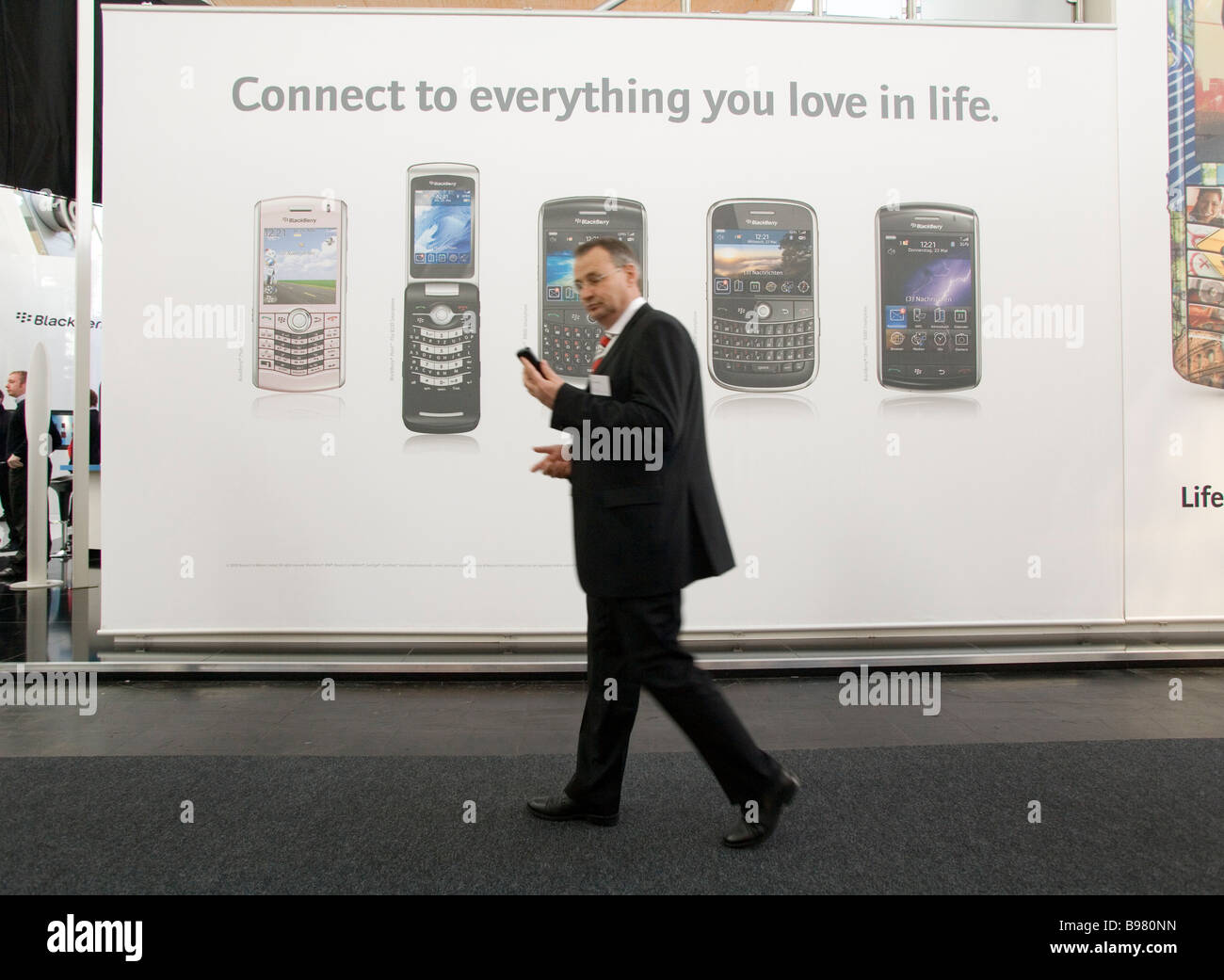 Il CeBIT imprenditore con smartphone nella parte anteriore di un poster pubblicitario per smartphone vari Foto Stock
