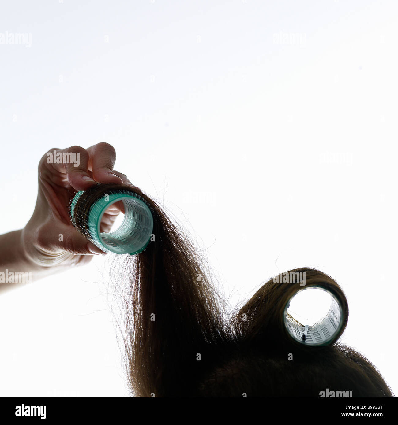 Giovane donna arricciare i capelli con rullo per capelli, close-up Foto Stock