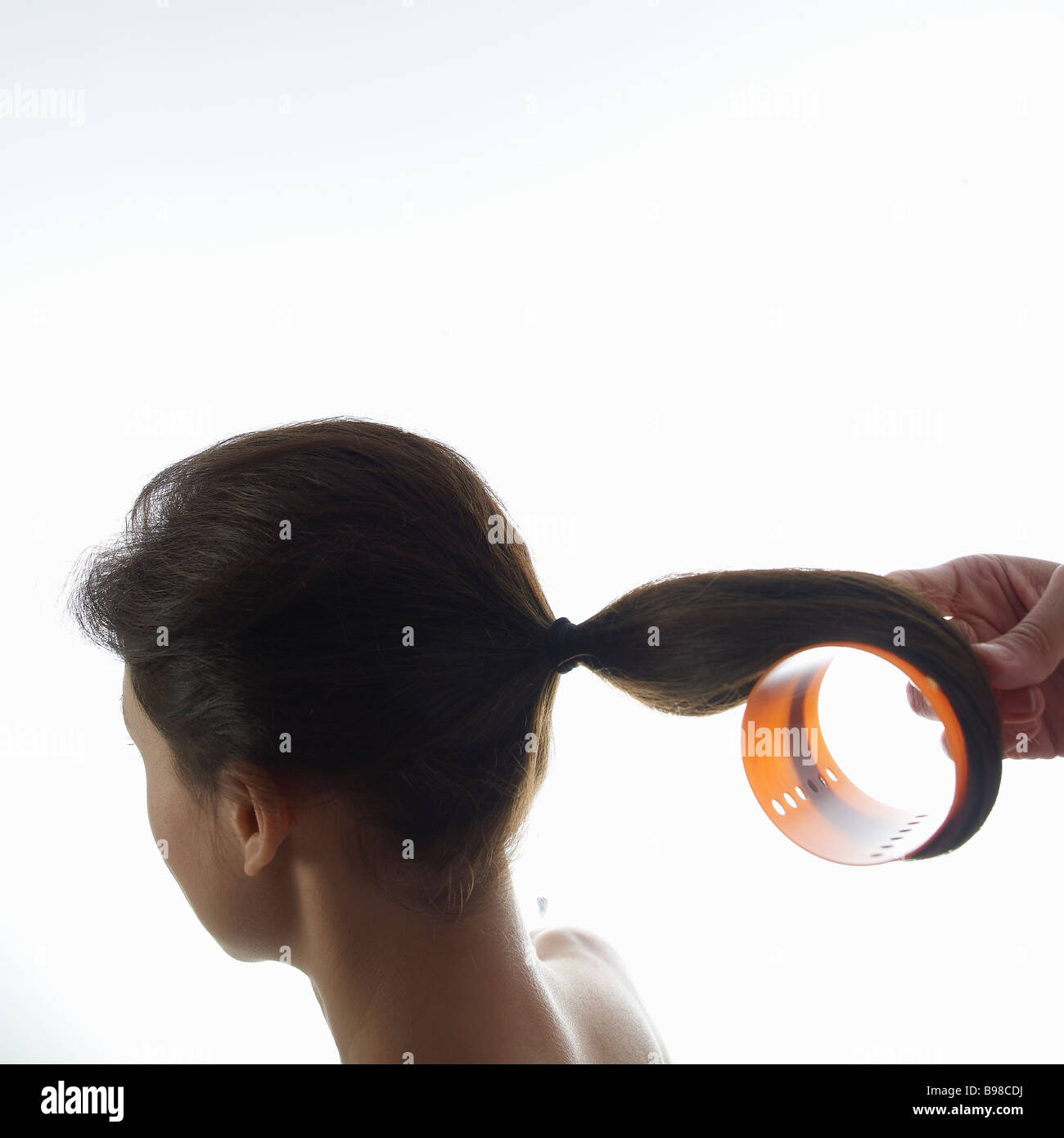 Giovane donna arricciare i capelli con rullo per capelli, close-up Foto Stock