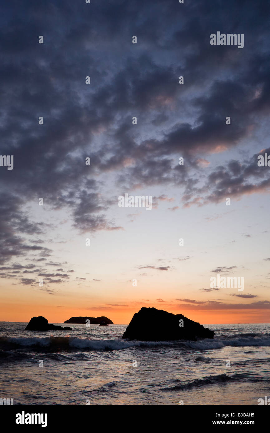 Drammatica viola e arancione sky con vista oceano si infrangono contro le rocce durante il tramonto a Playa Espadilla in Manuel Antonio, Costa Rica. Foto Stock