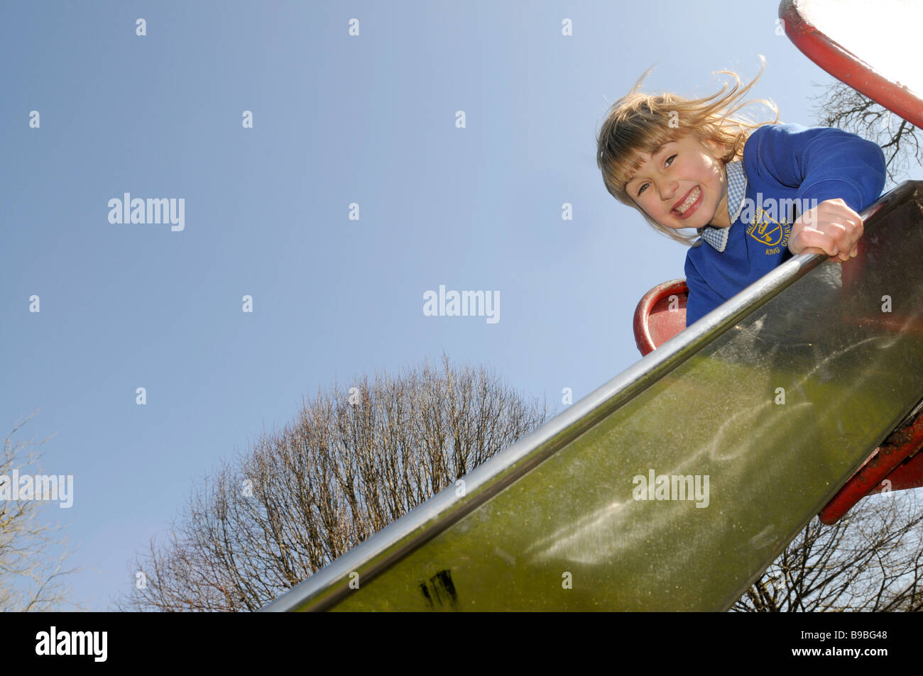 Un bambino di sei anni ragazza nella sua scuola uniforme su un parco giochi slitta Foto Stock