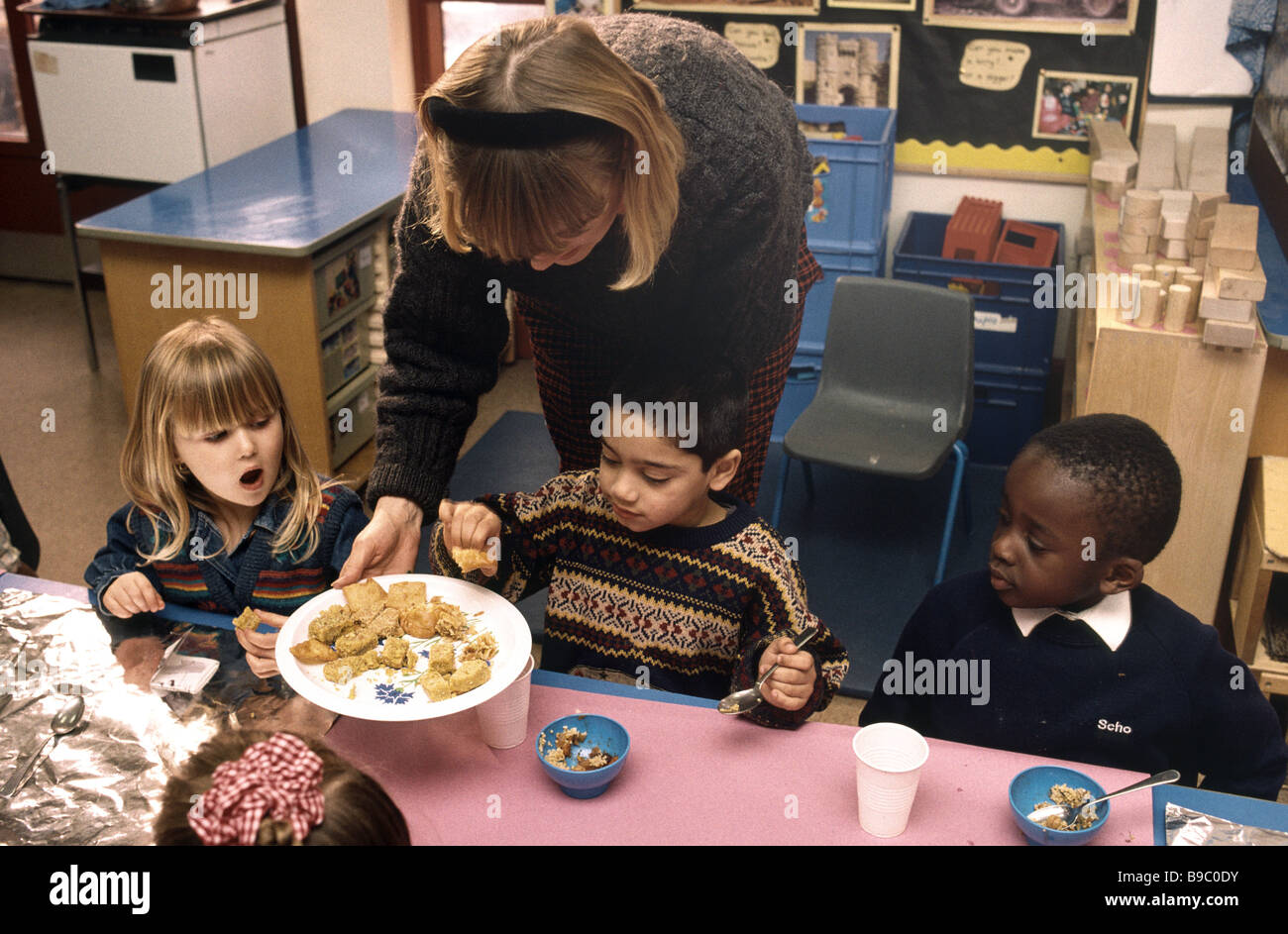 Scuola materna insegnante alimentazione dei bambini il pranzo Foto Stock