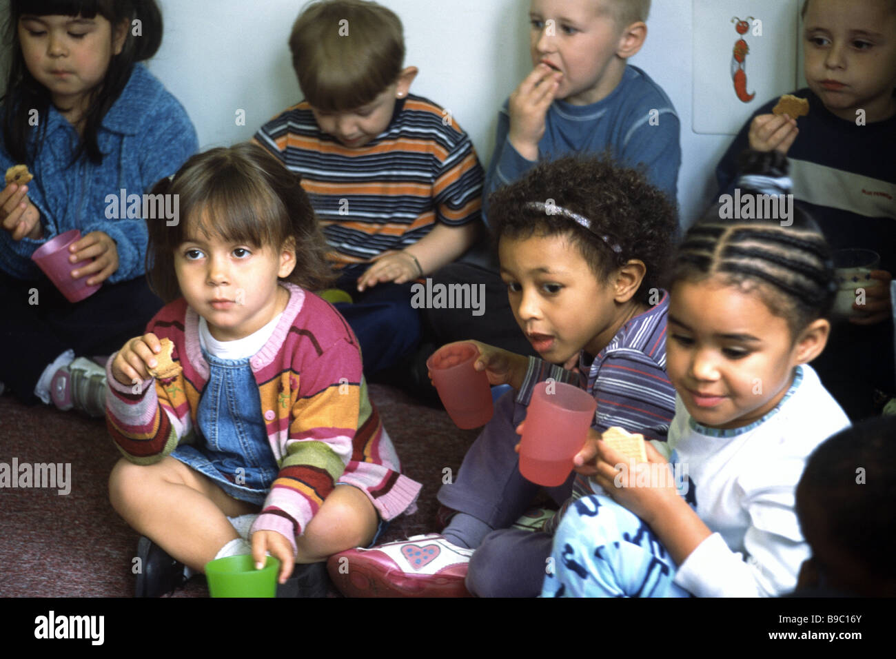 Bambini della scuola materna con un drink e un biscotto. Foto Stock