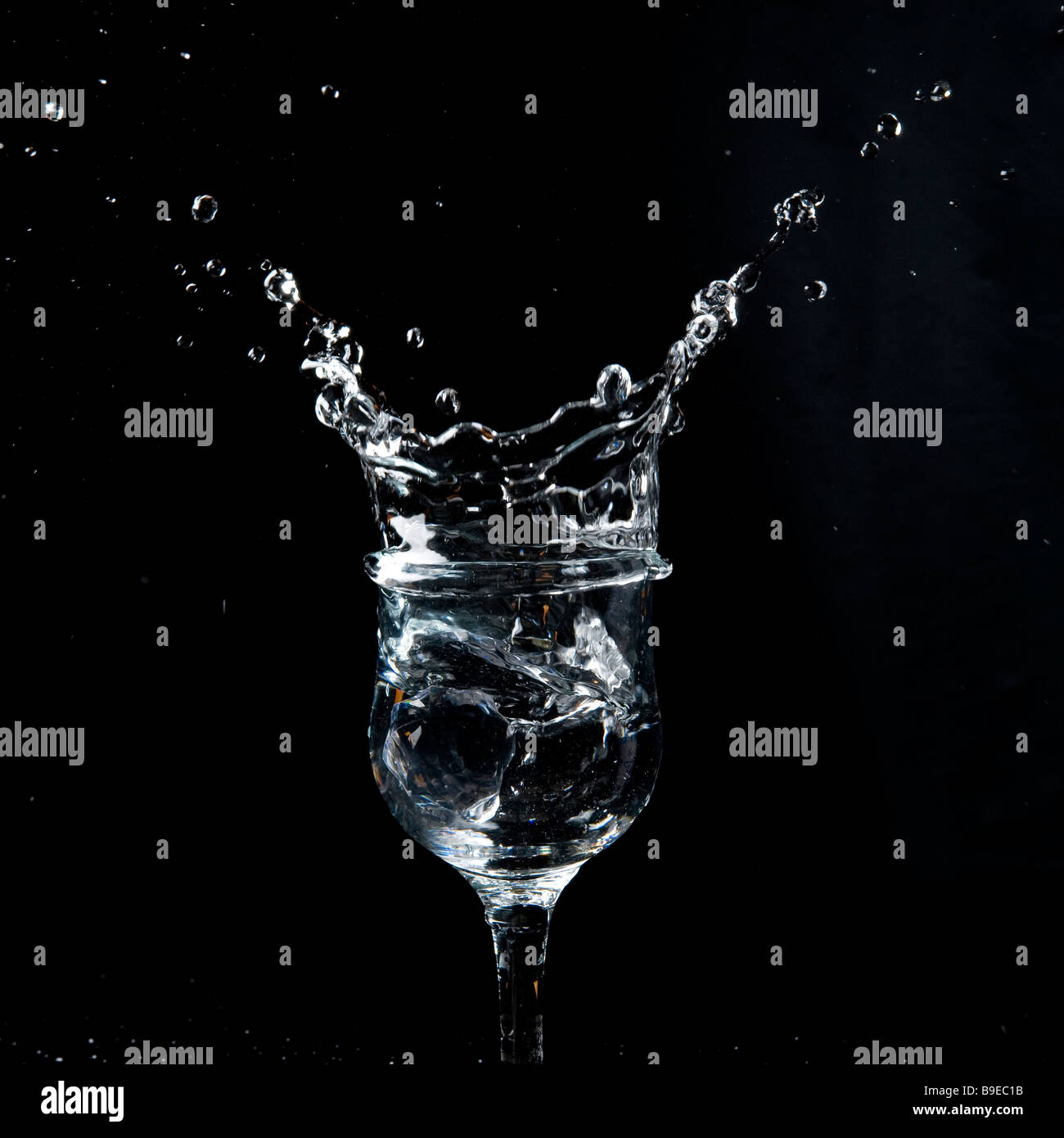 Bicchiere da vino fotografato su uno sfondo nero con caduta di acqua e ghiaccio effetto splash. Una corona di splash sorge sopra il vetro che riempie il fotogramma. Foto Stock