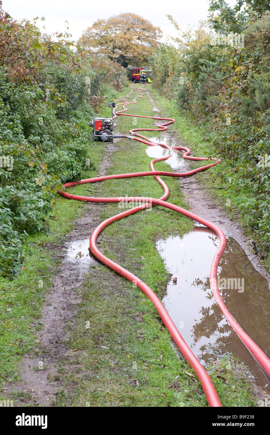 Più spezzoni di tubo antincendio e la luce di pompa portatile in una fattoria vicolo del paese. Formato verticale Foto Stock