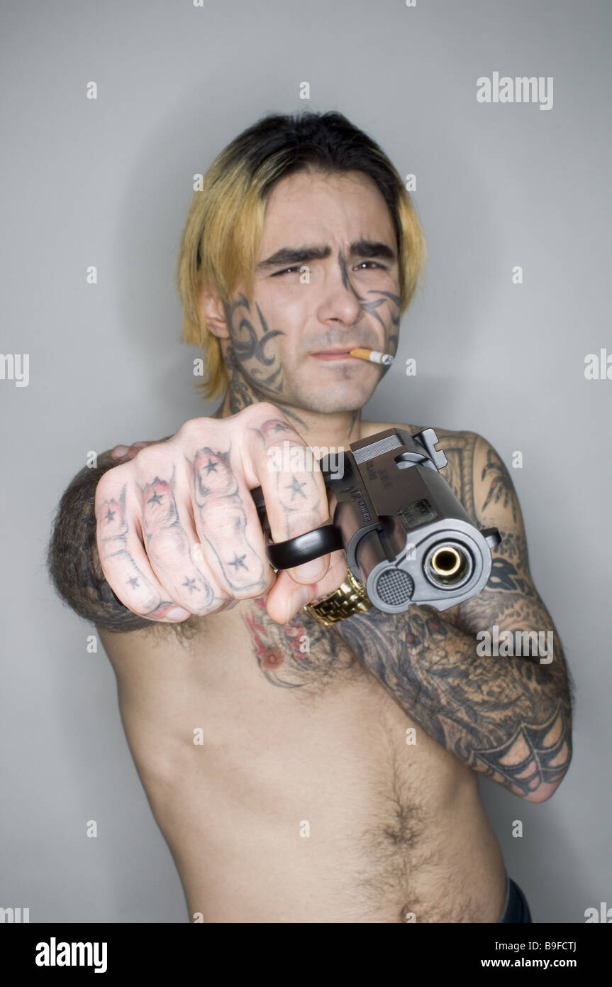 L'uomo giovane seriamente il corpo superiore liberamente tatuaggi sigaretta mira a pistola semi-ritratto la criminalità persone gangster face-tattoo tatuaggi Foto Stock