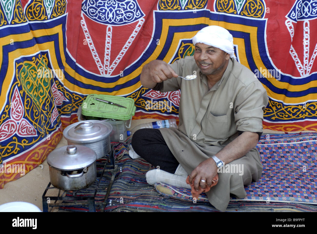 Egitto Desert Camp tenda beduina cuochi alimenti allegramente in Africa la gente uomo egiziani nomad seduta con le gambe incrociate fazzoletto copricapo Foto Stock