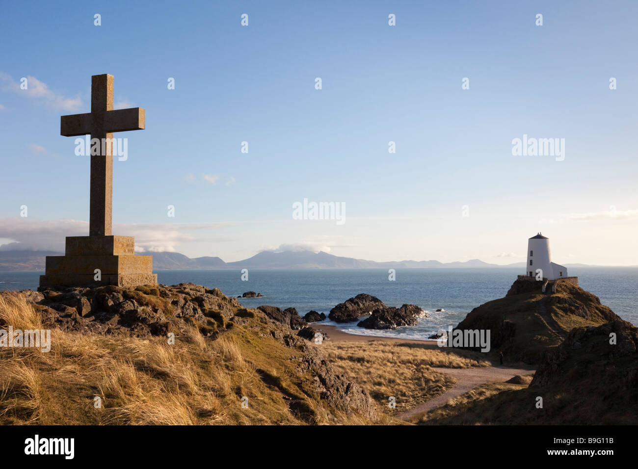 Anglesey North Wales UK croce di pietra memoriale e il vecchio faro Twr Mawr su rocky point di Ynys Llanddwyn Island in AONB Foto Stock