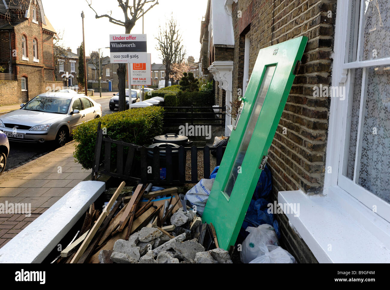 Rifiuti, macerie, rifiuti di cantiere al di fuori di una proprietà di essere rinnovato a Londra. Proprietà confinanti per la vendita in background. Foto Stock