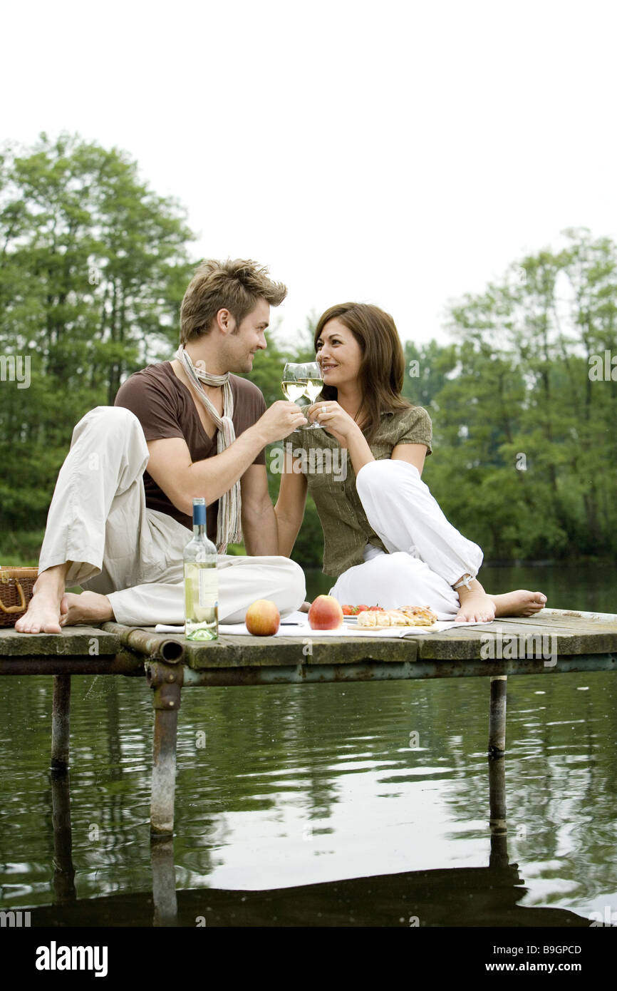 Il lago di Ponte di coppia innamorata seduta picnic clink bicchieri in appoggio a vasca da bagno lo sguardo di ponte-contatto snack Relax Tempo libero Foto Stock
