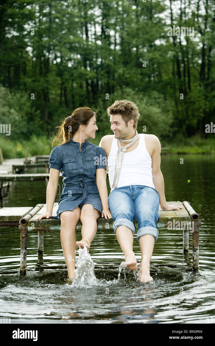 Il lago di coppia seduta ponte piedi acqua splash felice 20-30 anni il raffreddamento al di fuori del bagno-ponte lo sguardo a piedi nudi di rilassamento di contatto Foto Stock