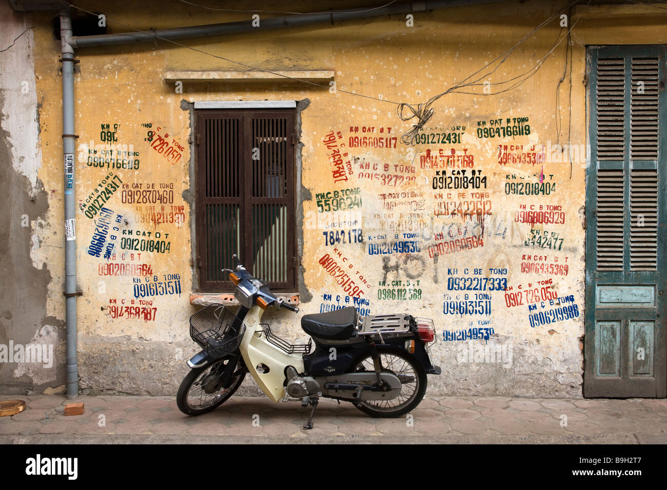 Moto parcheggiata aginst parete con Busness Graffitti Hanoi Vietnam Foto Stock