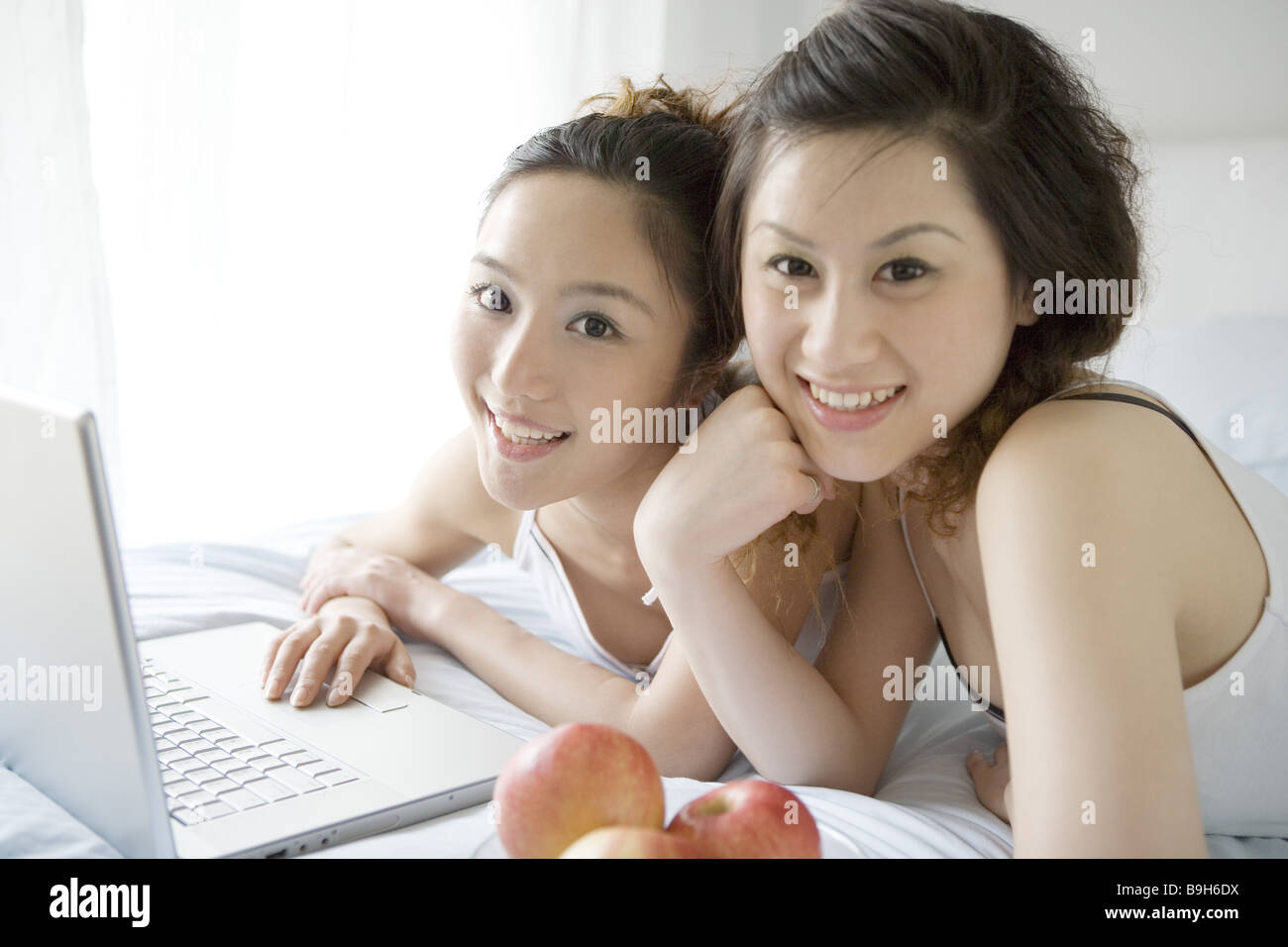Due giovani donne sdraiato sul letto con laptop e mele ritratto sorridente Foto Stock