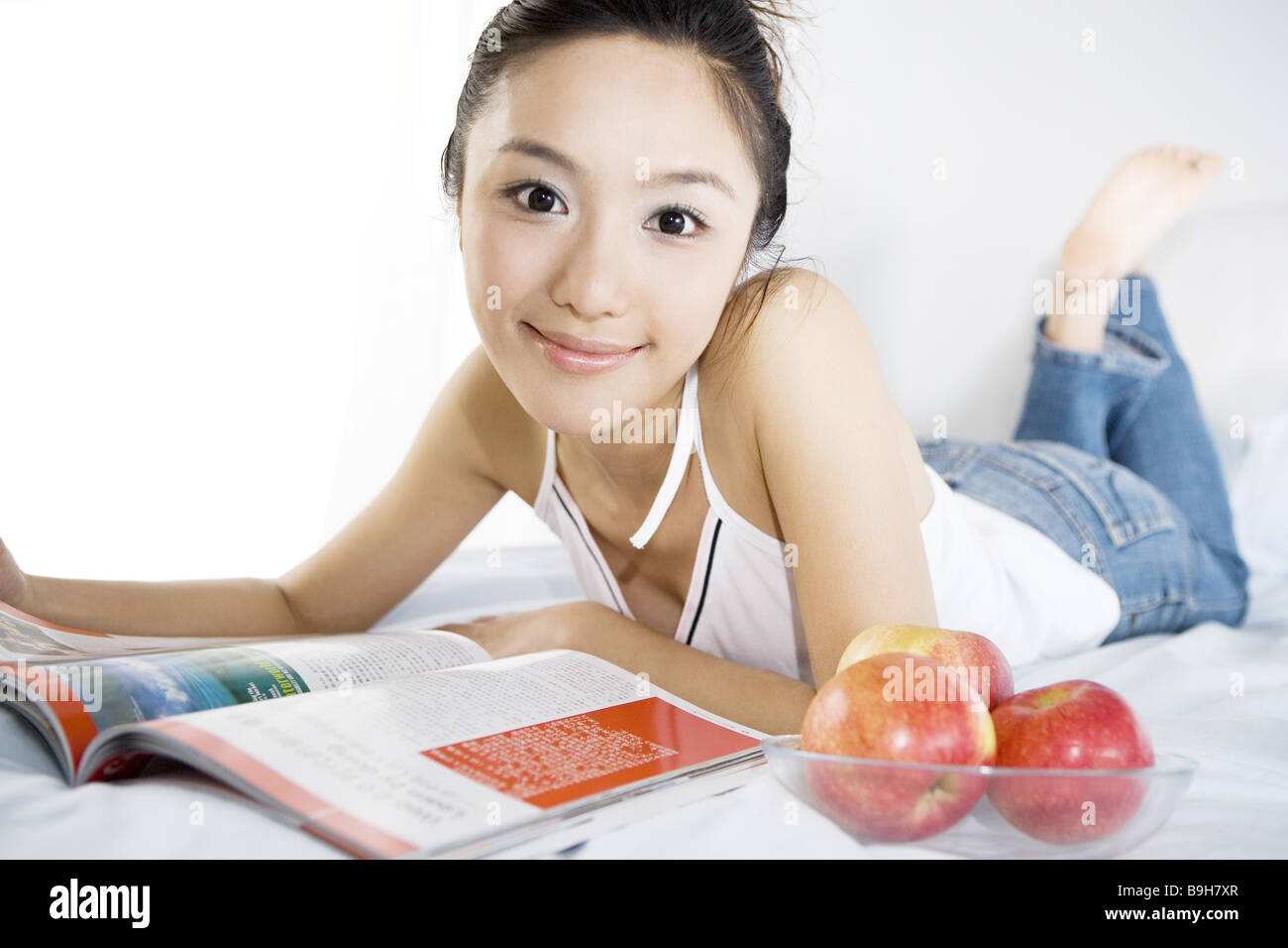 Una giovane donna giaceva sul letto con la rivista e le mele ritratto sorridente Foto Stock