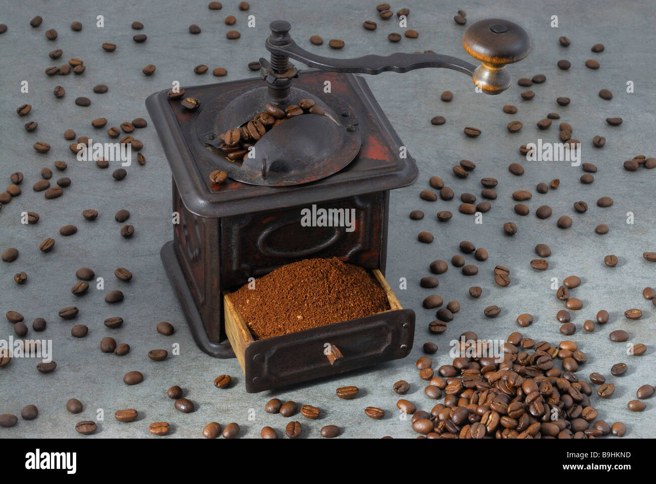 Metallo antico mulino di caffè con un cassetto pieno di caffè macinato, stando in piedi in mezzo sparsi i chicchi di caffè Foto Stock
