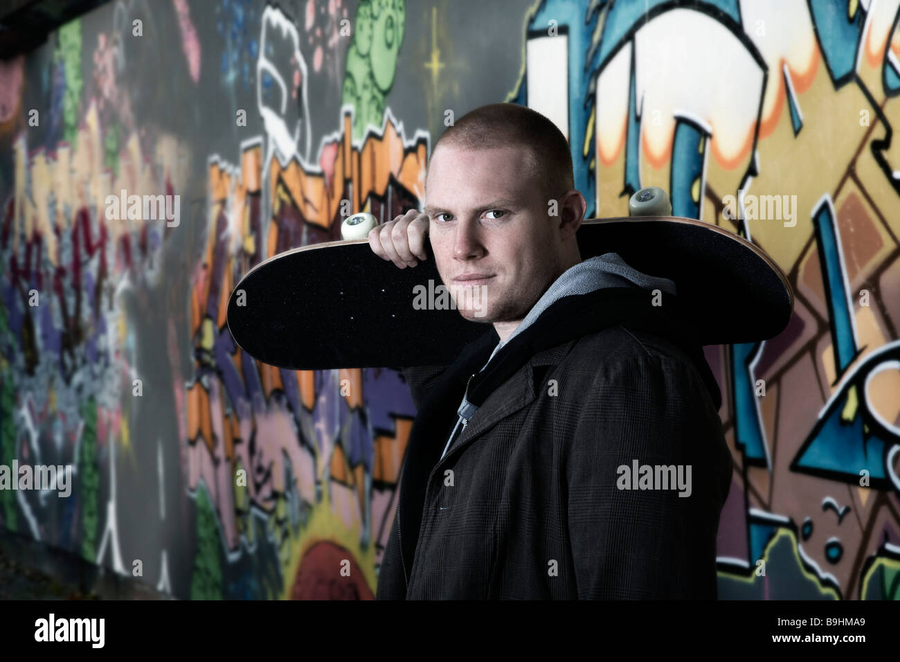 Giovane uomo con uno skateboard di fronte a un muro di graffiti, ritratto Foto Stock