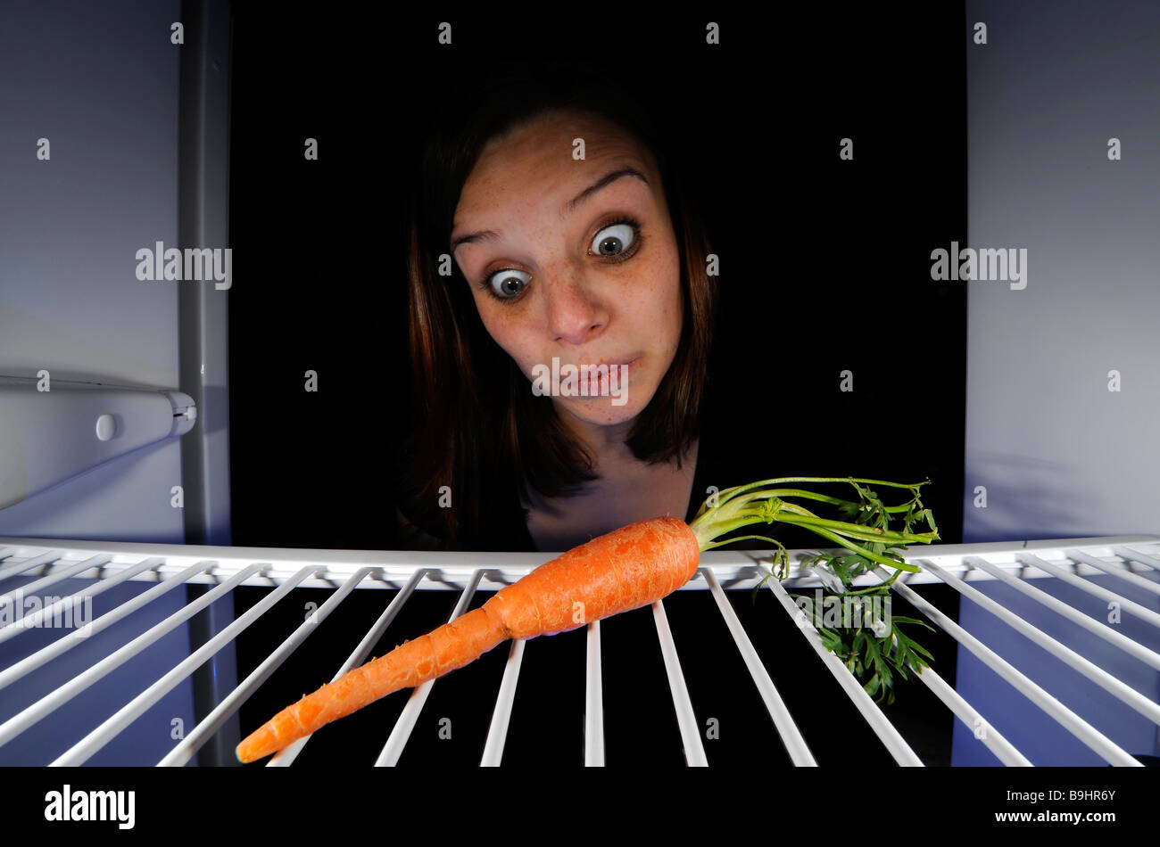 Giovane donna per quanto riguarda una singola carota in un frigorifero vuoto Foto Stock