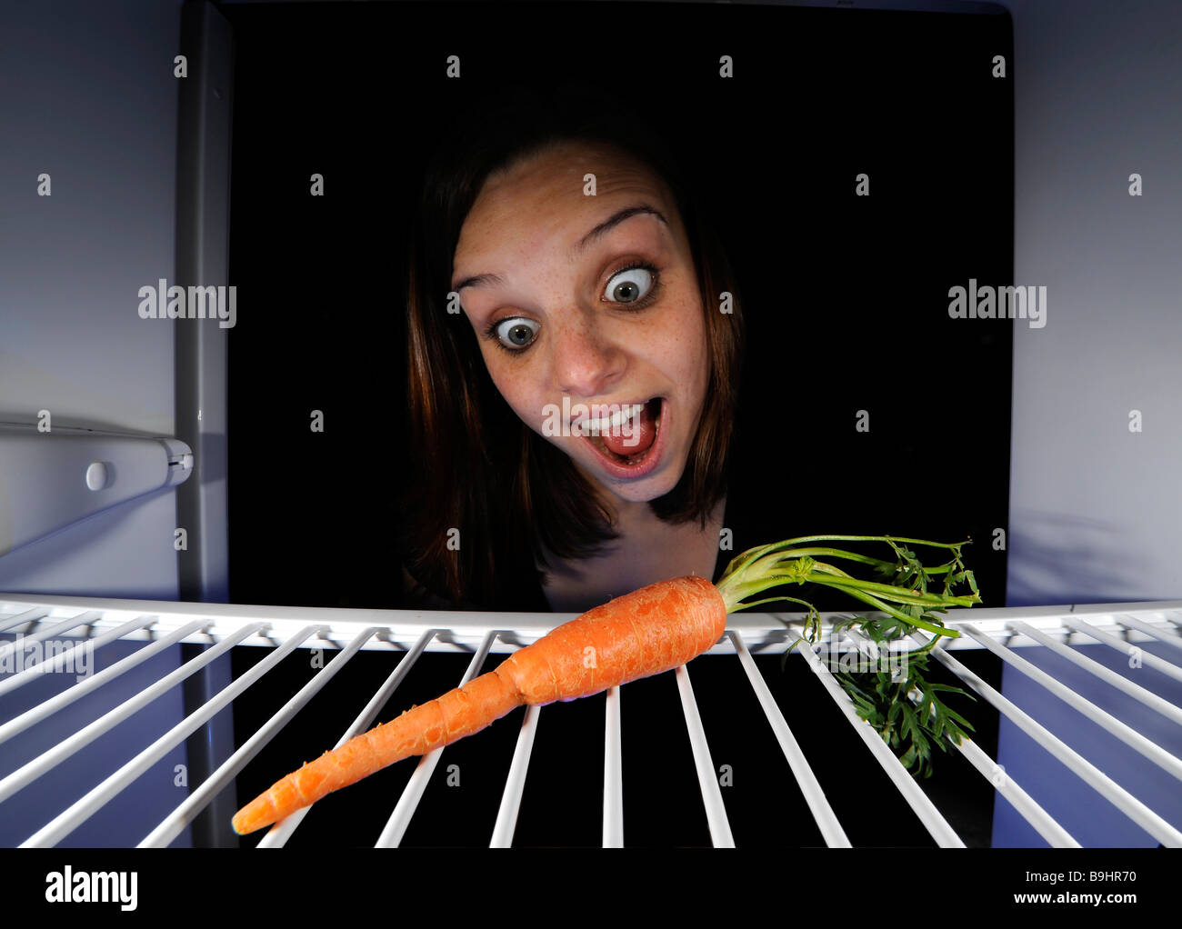 Giovane donna per quanto riguarda una singola carota in un frigorifero vuoto Foto Stock