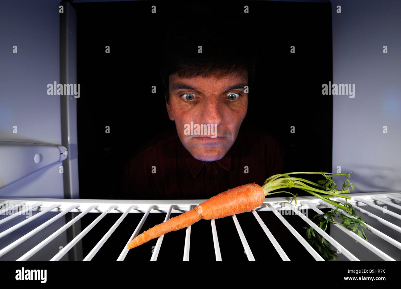 L'uomo per quanto riguarda una singola carota in un frigorifero vuoto Foto Stock