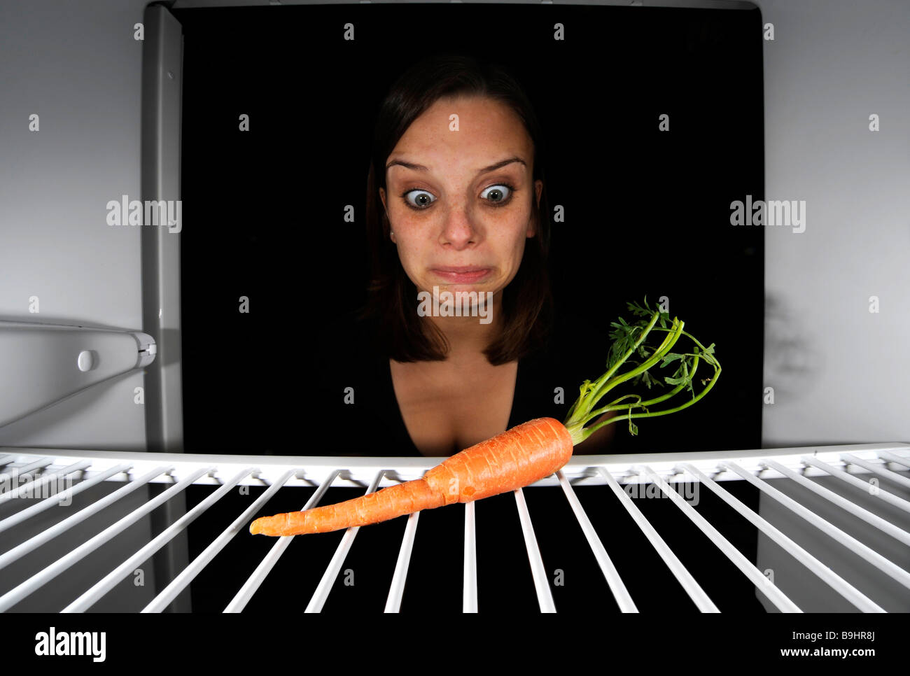 Giovane donna per quanto riguarda una singola carota in un frigorifero vuoto Foto Stock