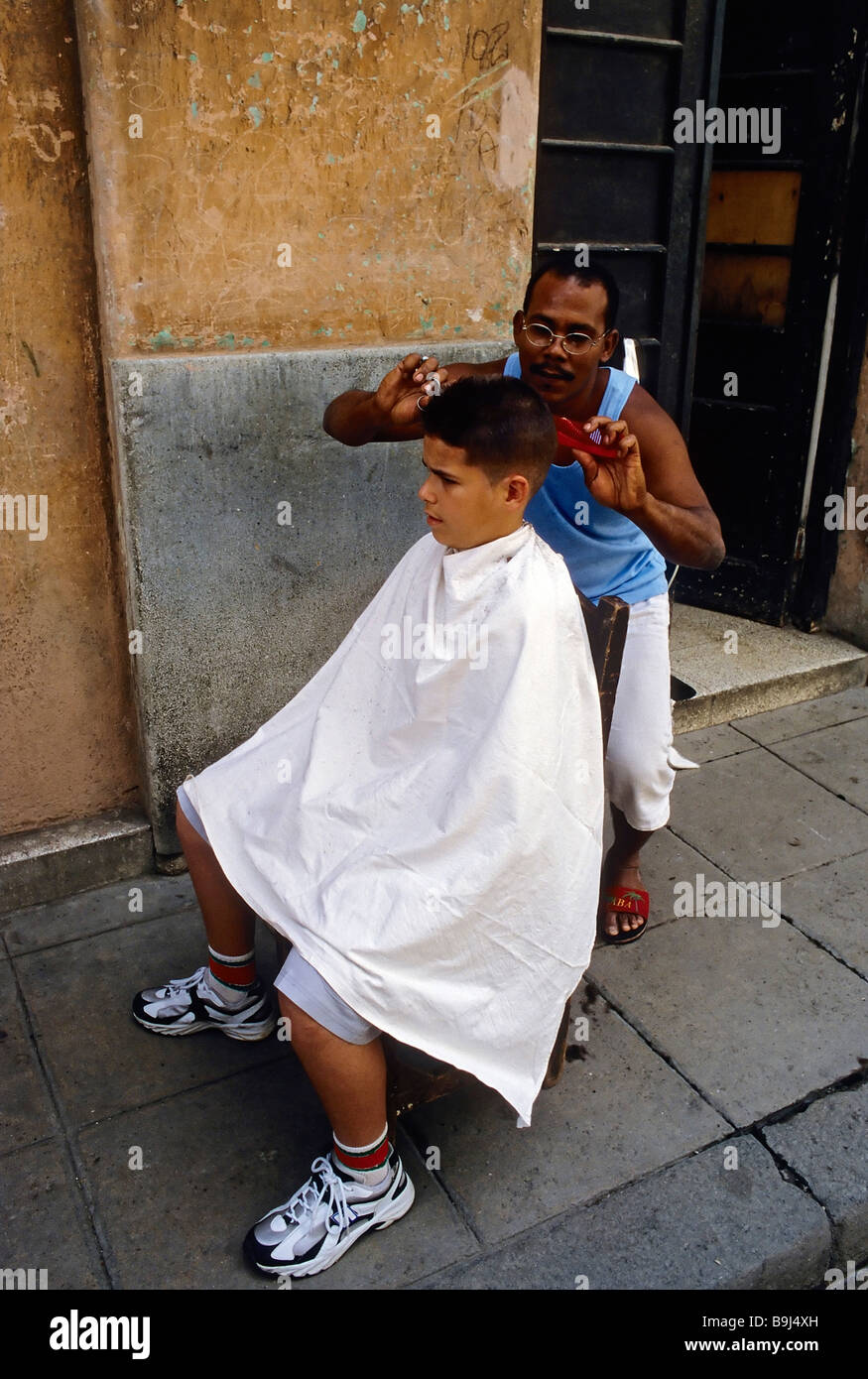 Parrucchiere cubano il taglio di un ragazzo in capelli sulla strada, La Habana Vieja, Havana, Cuba, Caraibi Foto Stock