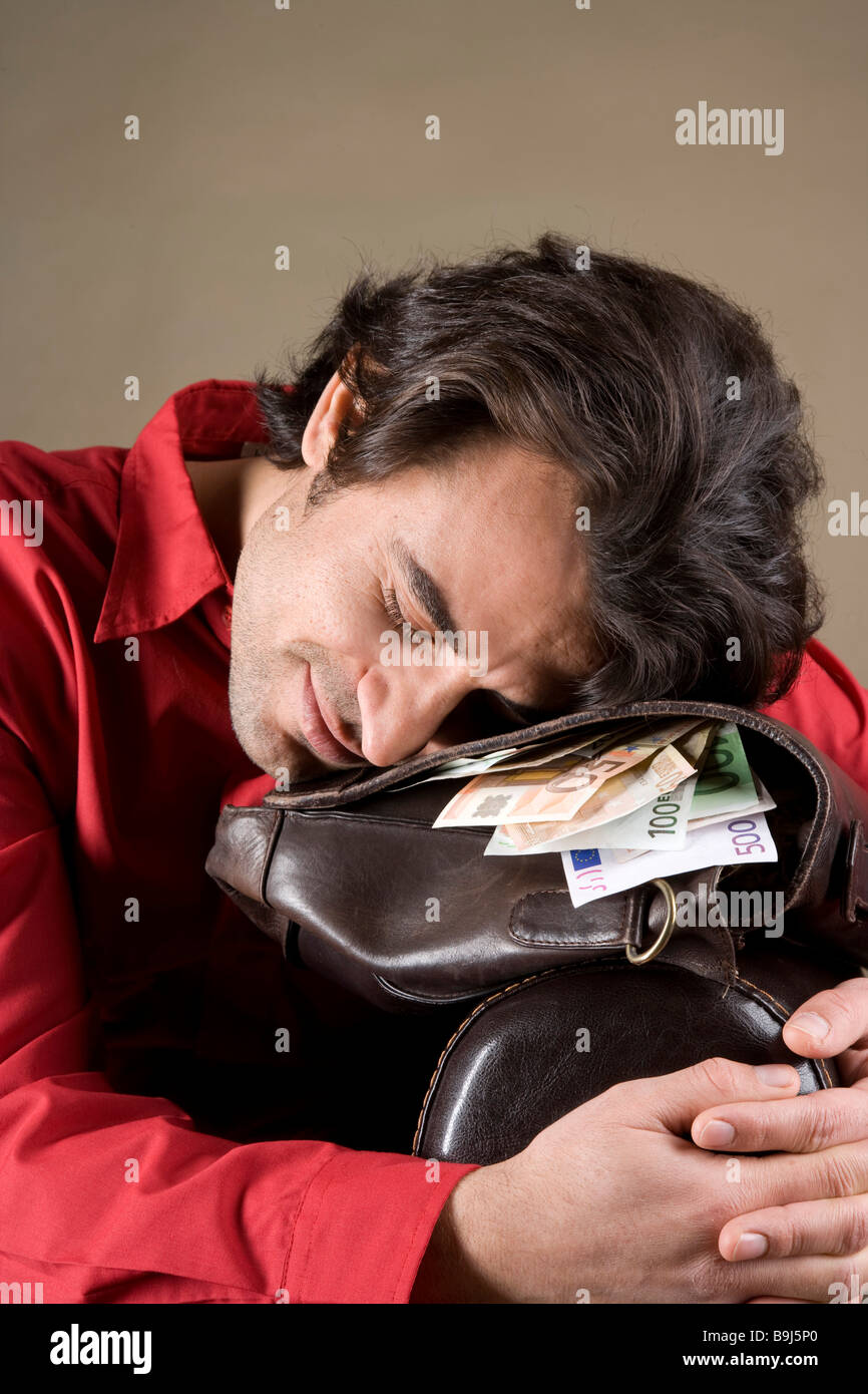 Giovane uomo contenuto in appoggio sulla sua borsa piena di denaro Foto Stock