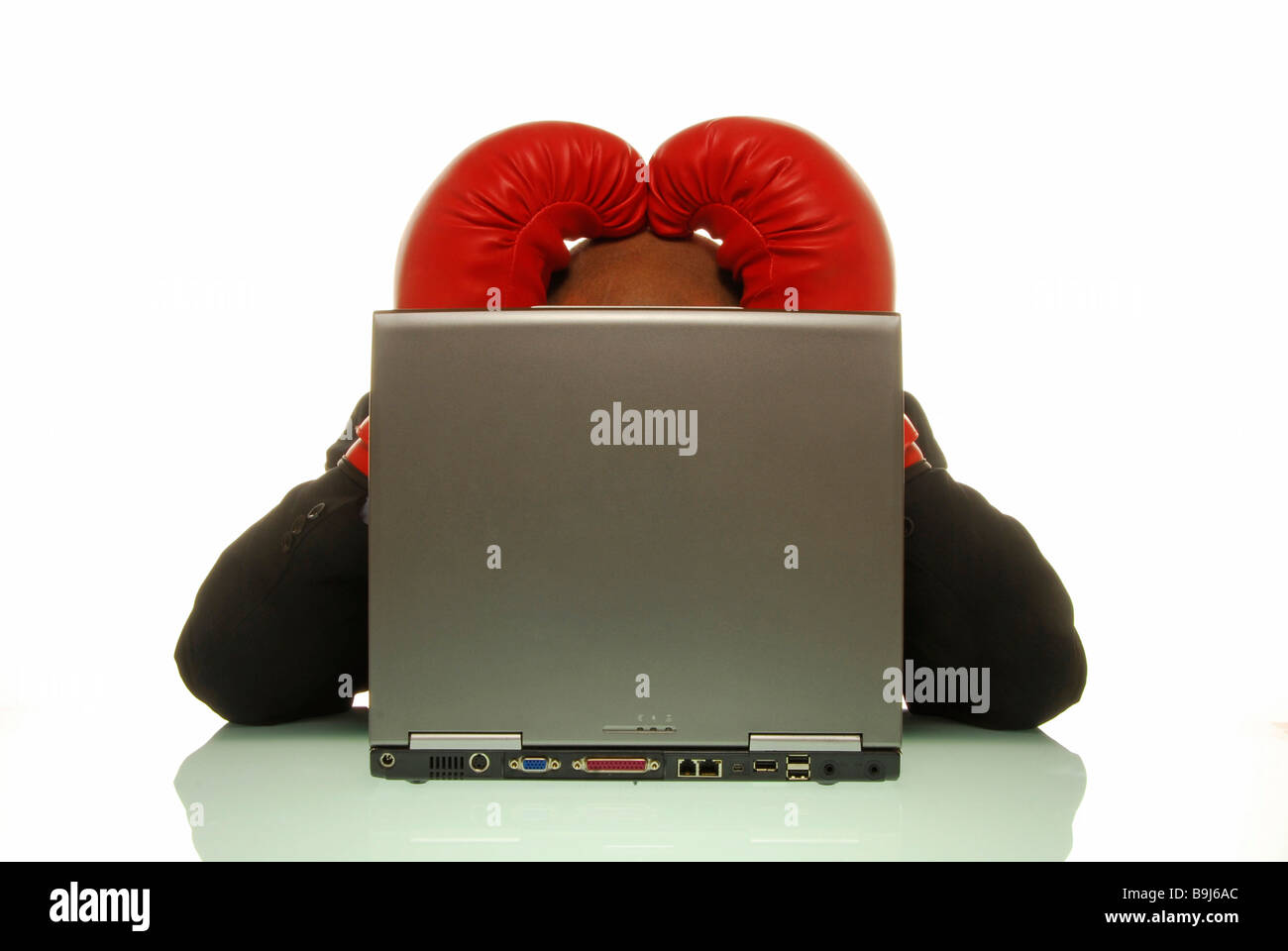 Imprenditore indossando guanti da boxe tenendo le mani alla testa dietro un computer portatile Foto Stock