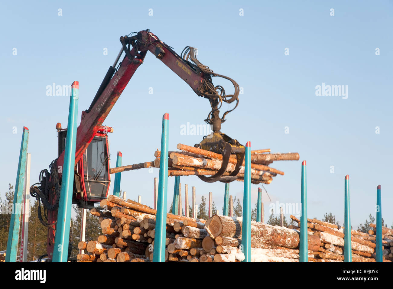 Camionista finlandese che utilizza gru per camion e tronchi di carico per i vagoni ferroviari di carico presso il deposito ferroviario di Inverno . Finlandia Foto Stock