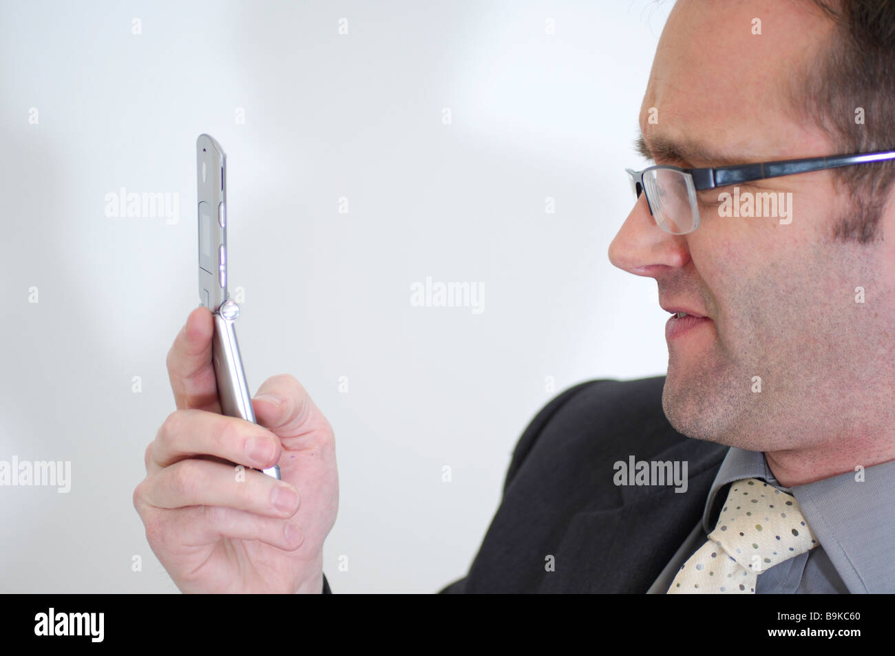 Vista laterale di imprenditore con occhiali controllo cellulare per i messaggi di testo Foto Stock