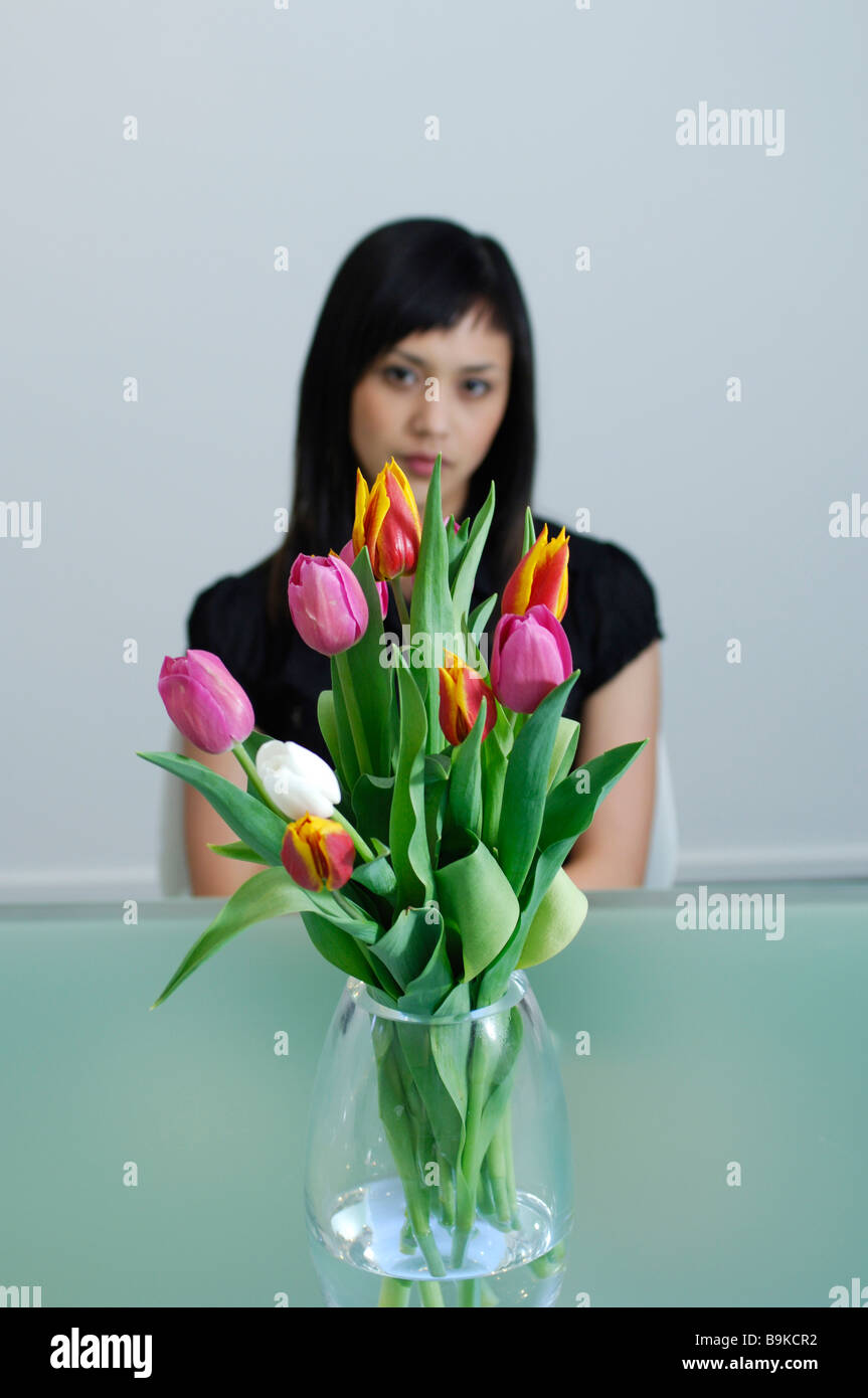 Triste guardando donna asiatica seduto dietro il vaso di fiori Foto Stock