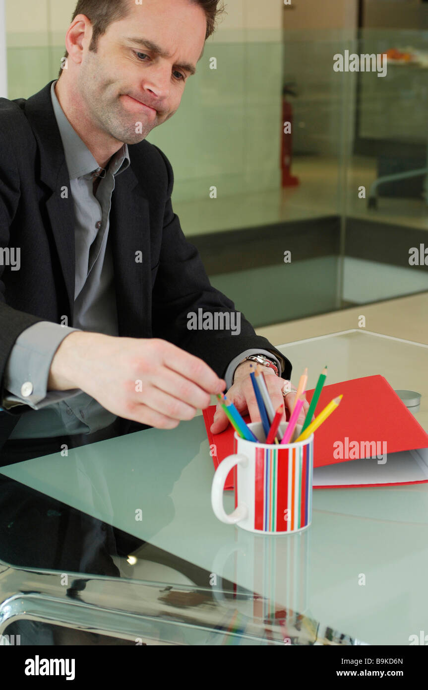Infastiditi dipendente cercando di prendere una matita dalla tazza sul tavolo Foto Stock