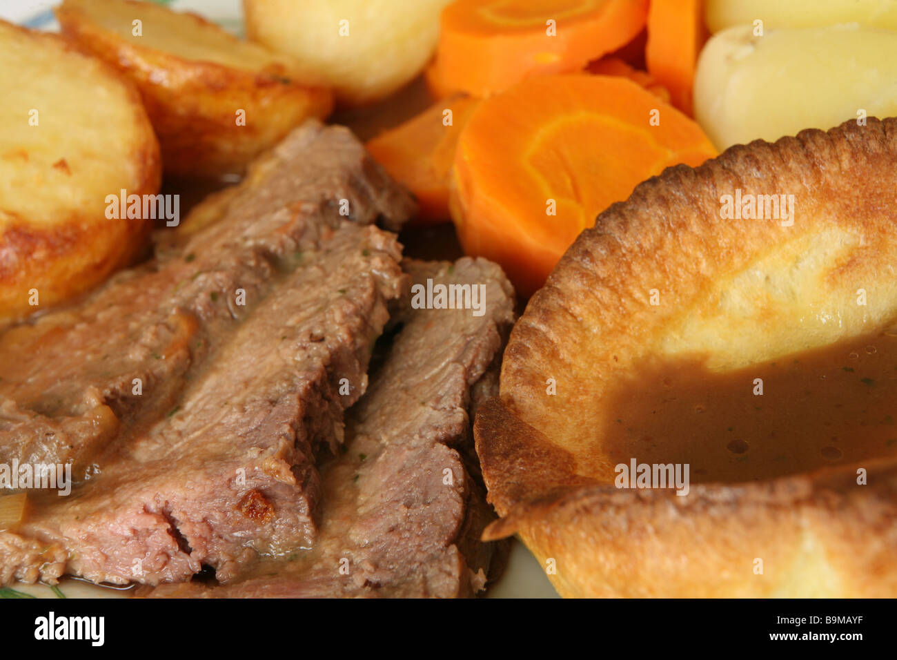 Extreme close-up su una cena di roast beef e Yorkshire pudding,con arrosti e bolliti di patate e carote. Foto Stock