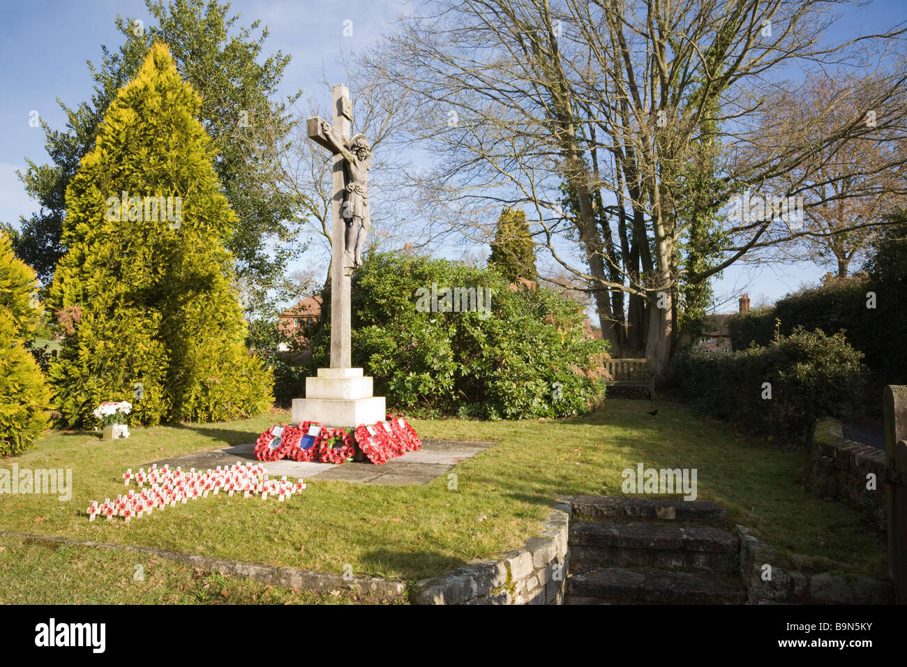 Pirbright Surrey in Inghilterra UK crocifisso di pietra memoriale di guerra con papavero rosso ghirlande e crocifissi nel sagrato della chiesa Foto Stock