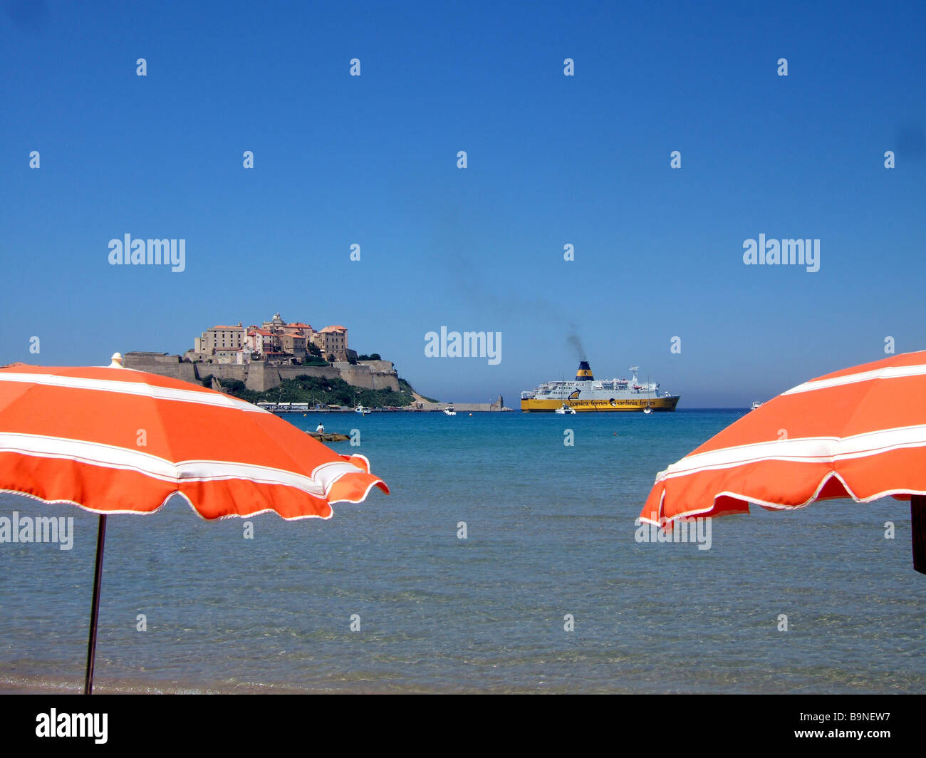 Di fronte al mare, spiaggia umberellas con la cittadella di Calvi e di una Corsica Ferries nave in background Calvi, Corsica, Francia. Foto Stock