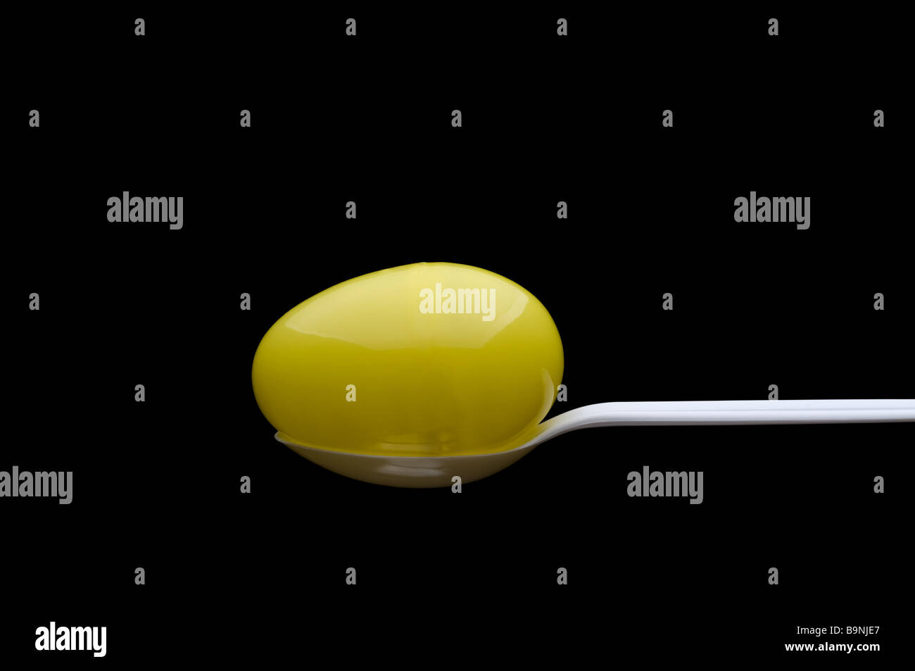 In plastica di colore giallo uovo di Pasqua su un cucchiaino di colore bianco con sfondo nero Foto Stock