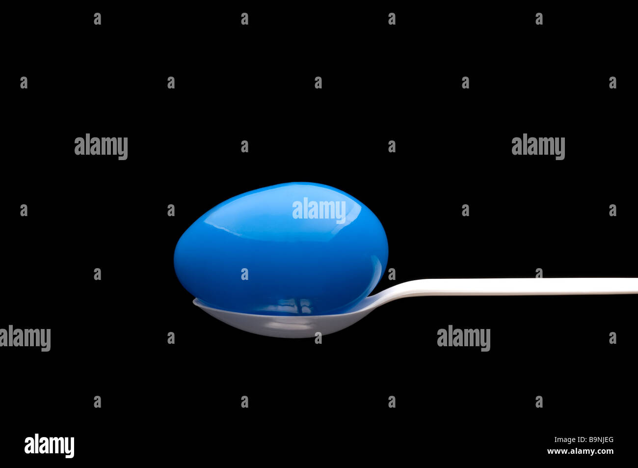 Plastica blu uovo di Pasqua su un cucchiaino di colore bianco con sfondo nero Foto Stock