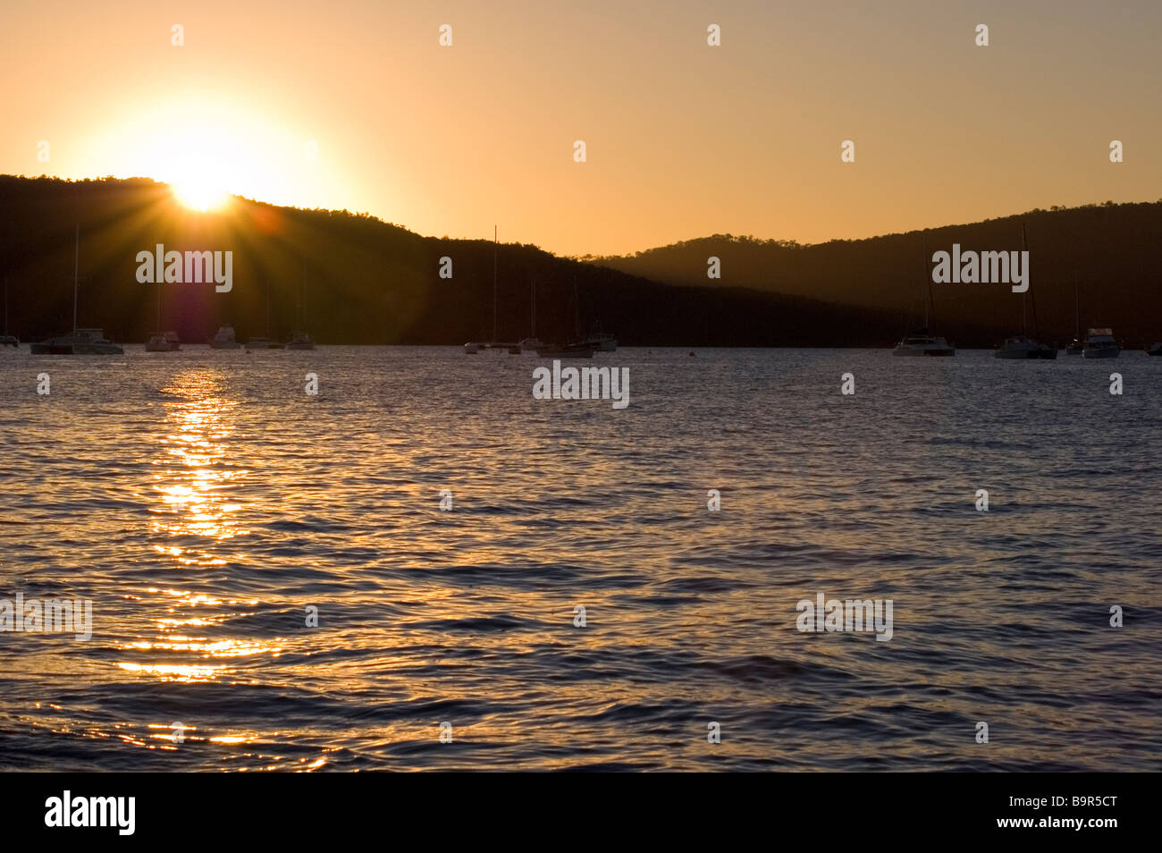 Il sole che tramonta dietro le colline sulla costa, Airlie Beach, Queensland, Australia Foto Stock