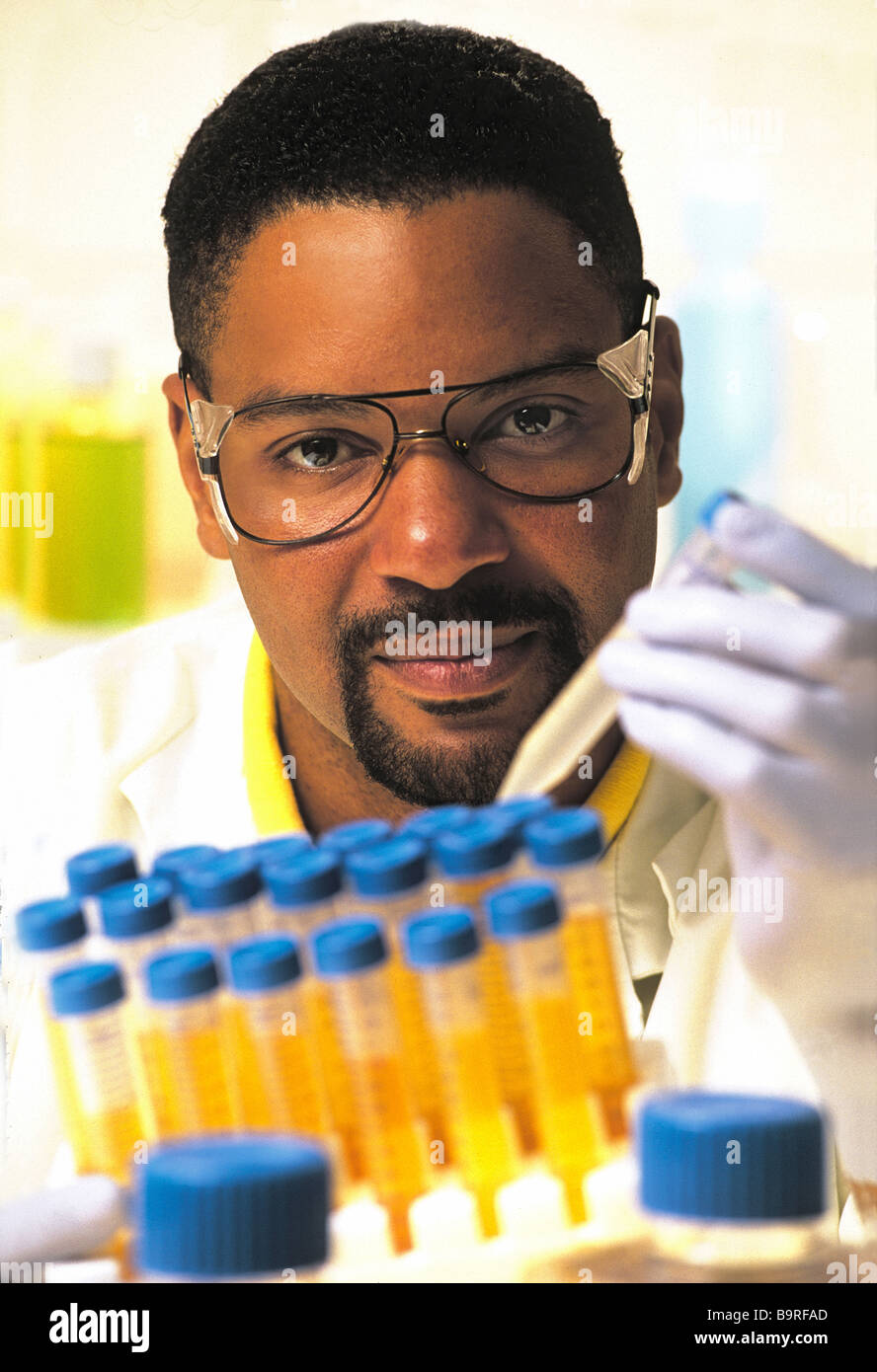 Maschio americano africano tecnico di laboratorio nel laboratorio di ricerca, tenendo le provette per la prova,indossando labcoat bianco e occhiali di sicurezza. Foto Stock