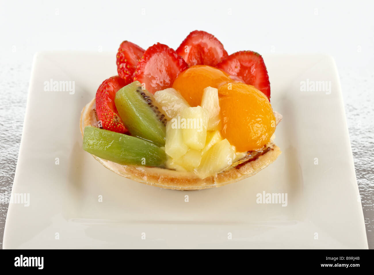 Vetrata flan di frutta su una piastra bianca con una miscela di frutta di stagione Foto Stock